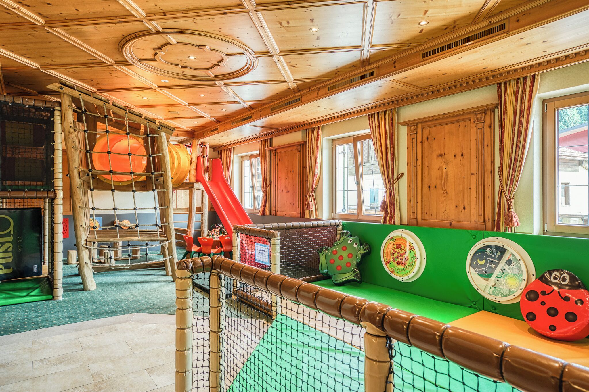 A play area with a wooden play structure, a slide, and colorful cushions.