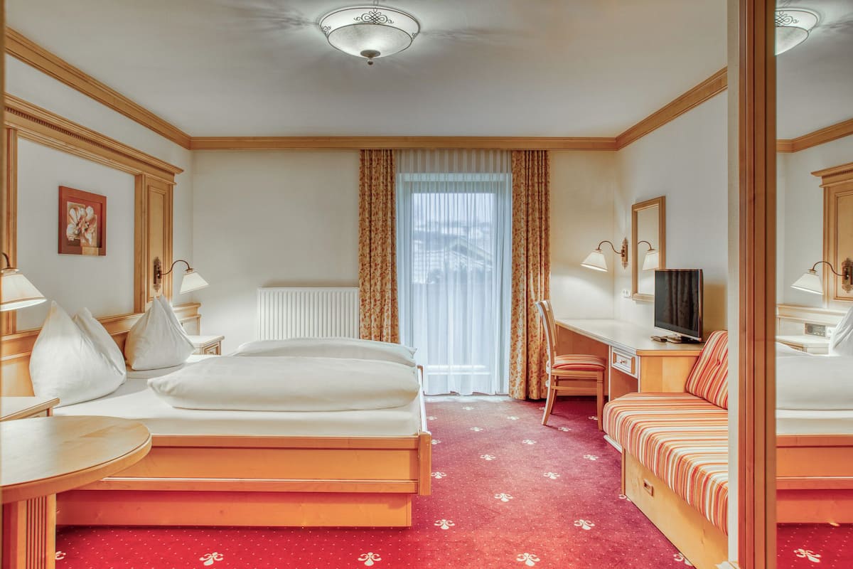 A hotel room with a bed, a desk, a chair, a television, and a window with curtains.