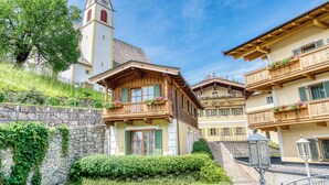 Un edificio de estilo alpino tradicional con muro de piedra, balcones de madera con macetas de flores y una torre del reloj.