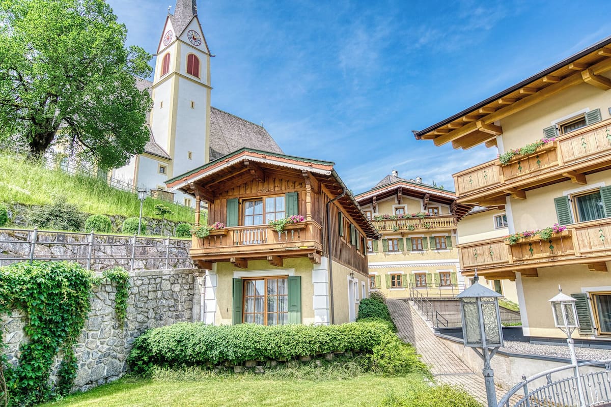 A traditional Alpine-style building with a stone wall, wooden balconies with flower boxes, and a clock tower.