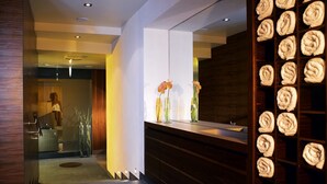 A modern hotel lobby with a reception desk, a large mirror, and a wall with rolled towels. - Hotel Solstein (Seefeld in Tirol)