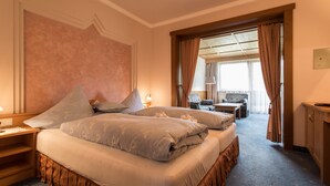 A hotel room with two beds, a wooden desk, a chair, and a view of the outside through a large window. - Hotel Solstein (Seefeld in Tirol)