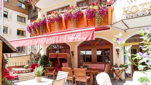 Ett hotell med uteservering, blomsterkorgar och ett rött markis.