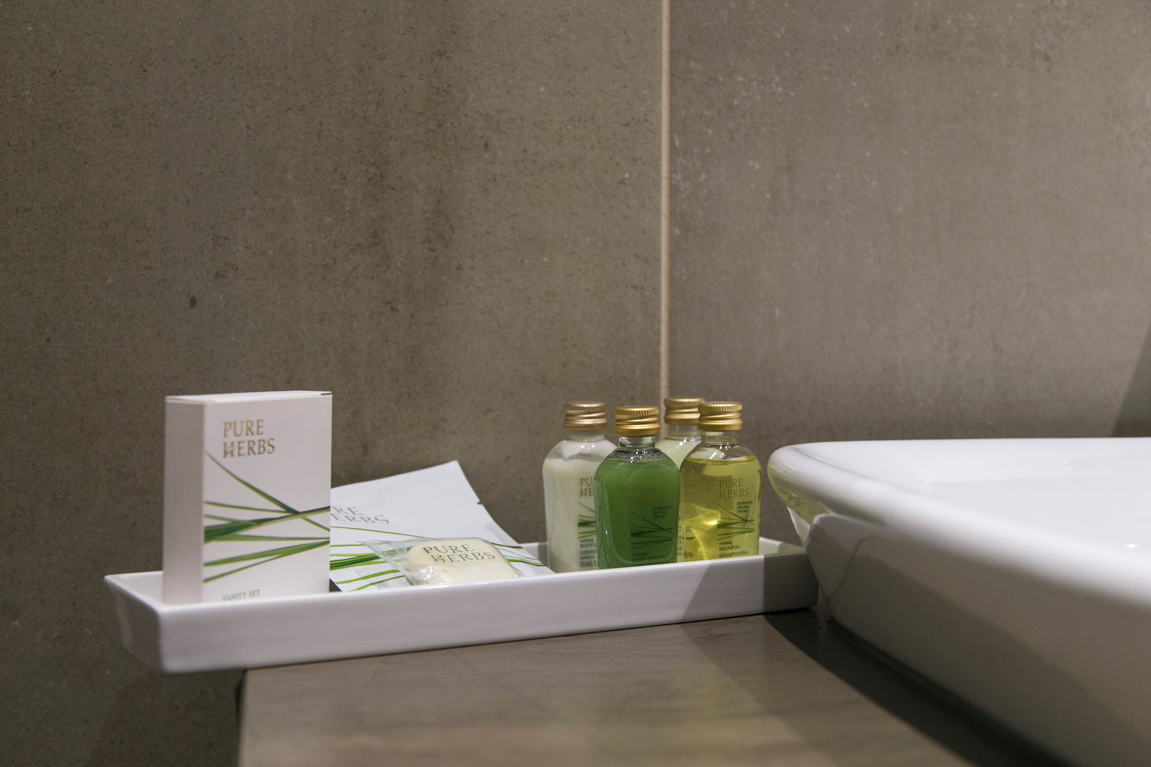 Casa de banho com lavatório branco, espelho e prateleira com o rótulo 'PURE HERBS' e três frascos.