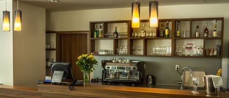 A bar area with a coffee machine, shelves with bottles, and a vase with yellow flowers.