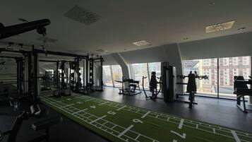 A gym with various exercise equipment, a green turf running track, and large windows offering views of buildings.