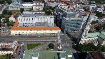 An aerial view of a city with a prominent building featuring a large red roof and multiple floors, surrounded by other buildings and streets.