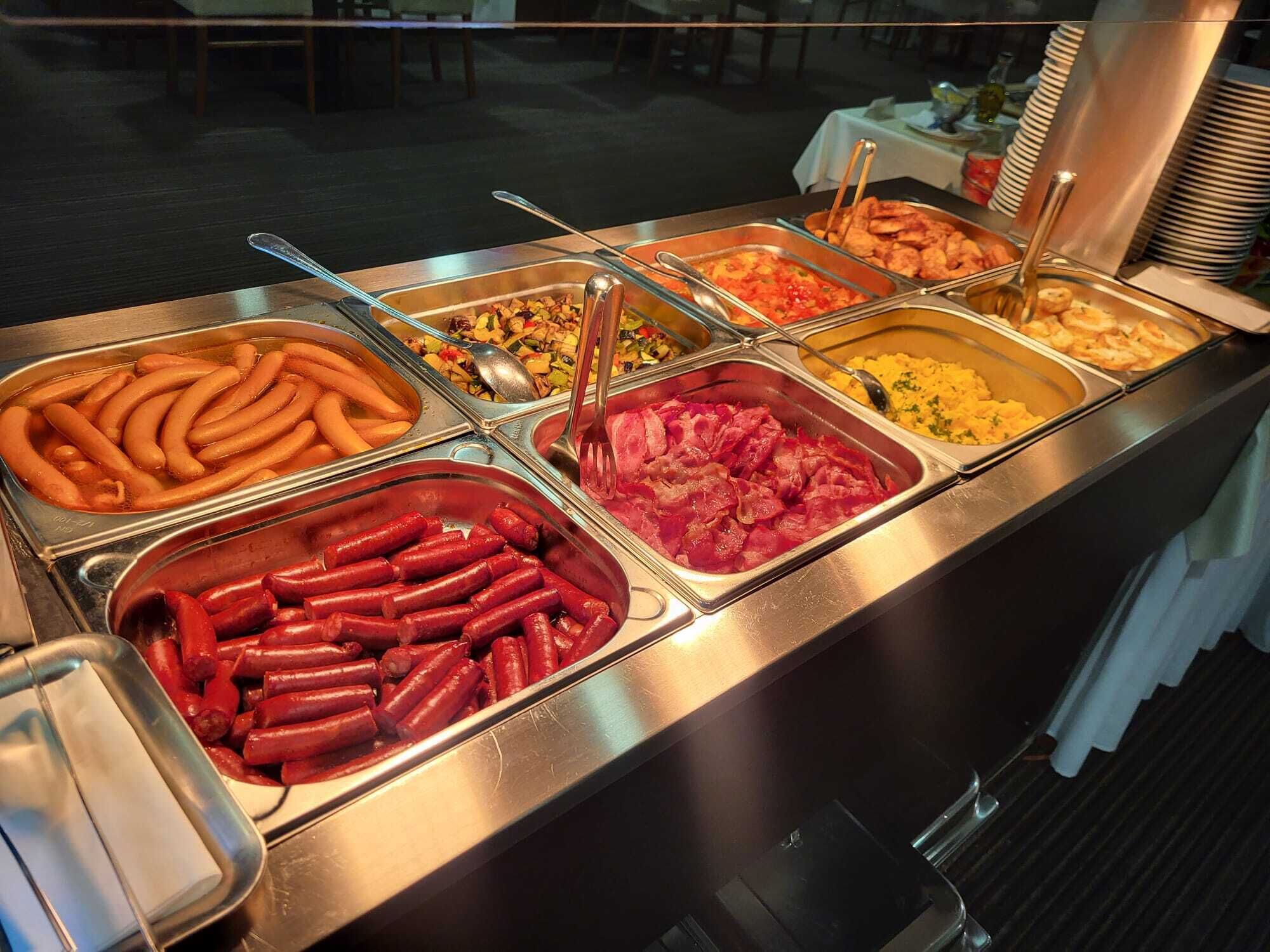 A buffet with various food options including sausages, a salad, and scrambled eggs.
