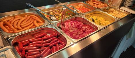 A buffet with various food options including sausages, a salad, and scrambled eggs.