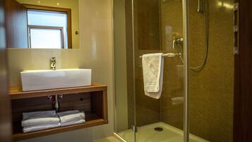 Een moderne badkamer met een douchecabine van glas, een witte wastafel en een houten meubel.