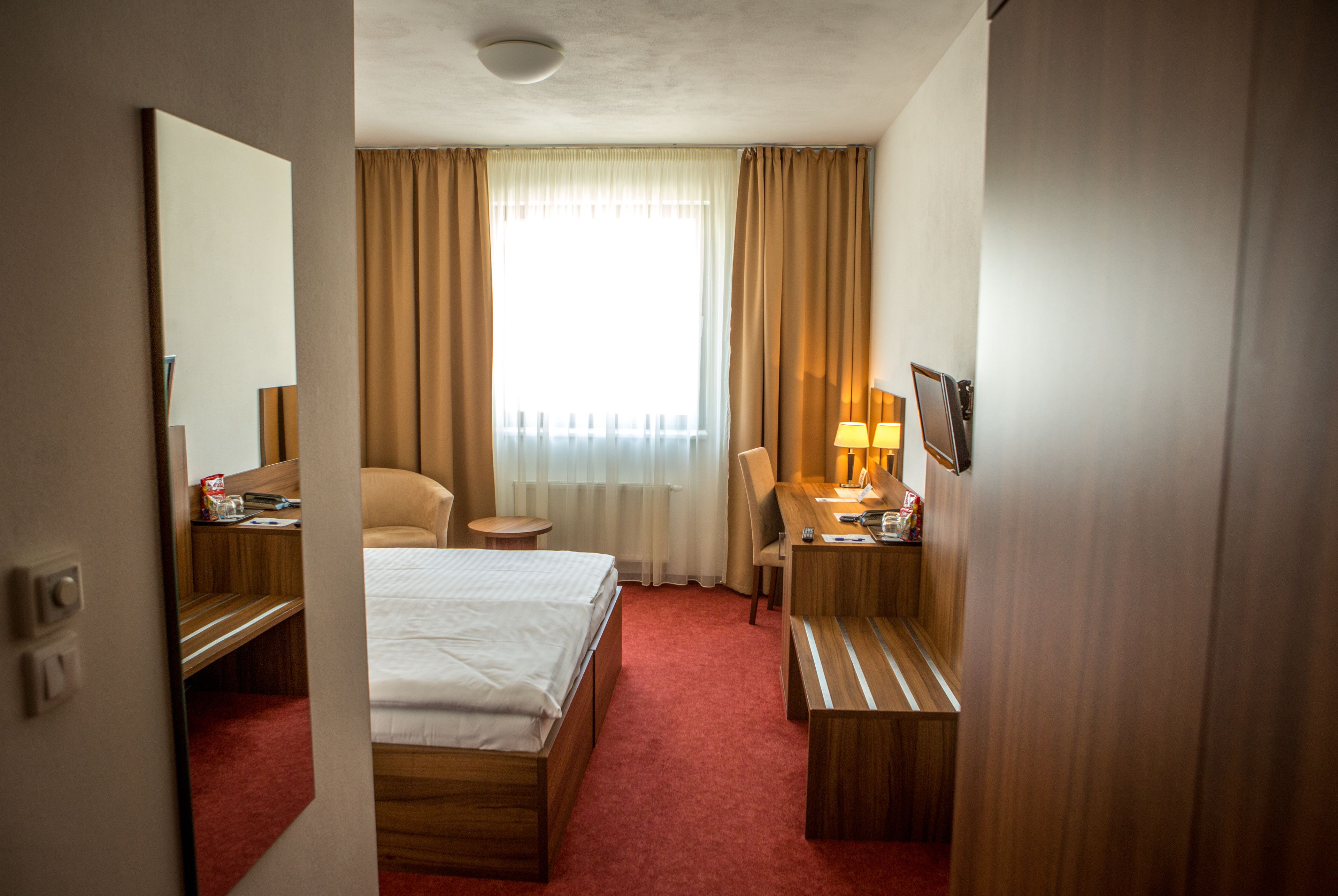 A hotel room with a bed, a desk, a chair, a small table, and a window with curtains.