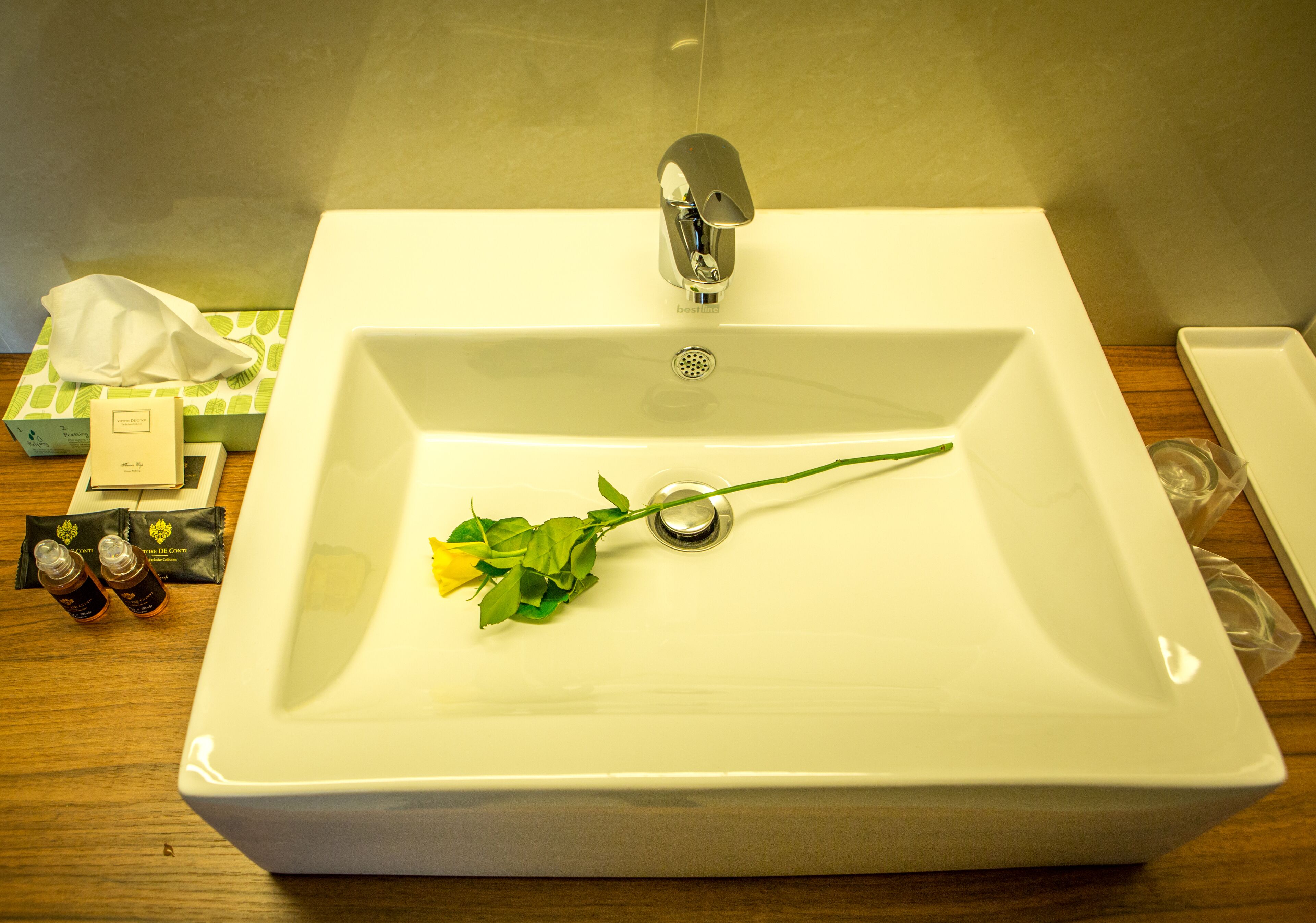 A bathroom sink with a single rose placed on it.