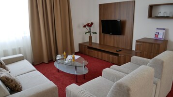 Habitación de hotel con televisión, mueble de madera y una mesa de centro de vidrio con tazas y una botella.