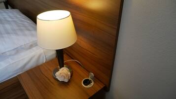 A wooden bedside table with a lamp, a rose, and a small round object.