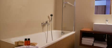 A bathroom with a bathtub, a shower, a sink, and a mirror. There are toiletries on the edge of the bathtub.
