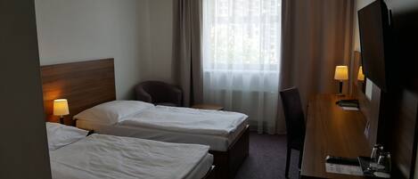 A hotel room with two beds, a wooden desk with a lamp, a chair, and a TV.
