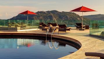 A poolside area with lounge chairs and umbrellas, surrounded by glass walls and a mountainous backdrop.