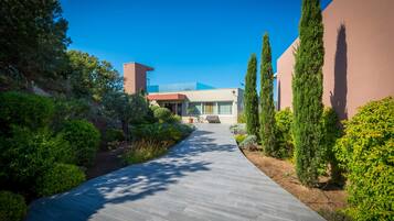 Un edificio moderno con un sendero pavimentado que lleva a la entrada, rodeado de vegetación y árboles altos.