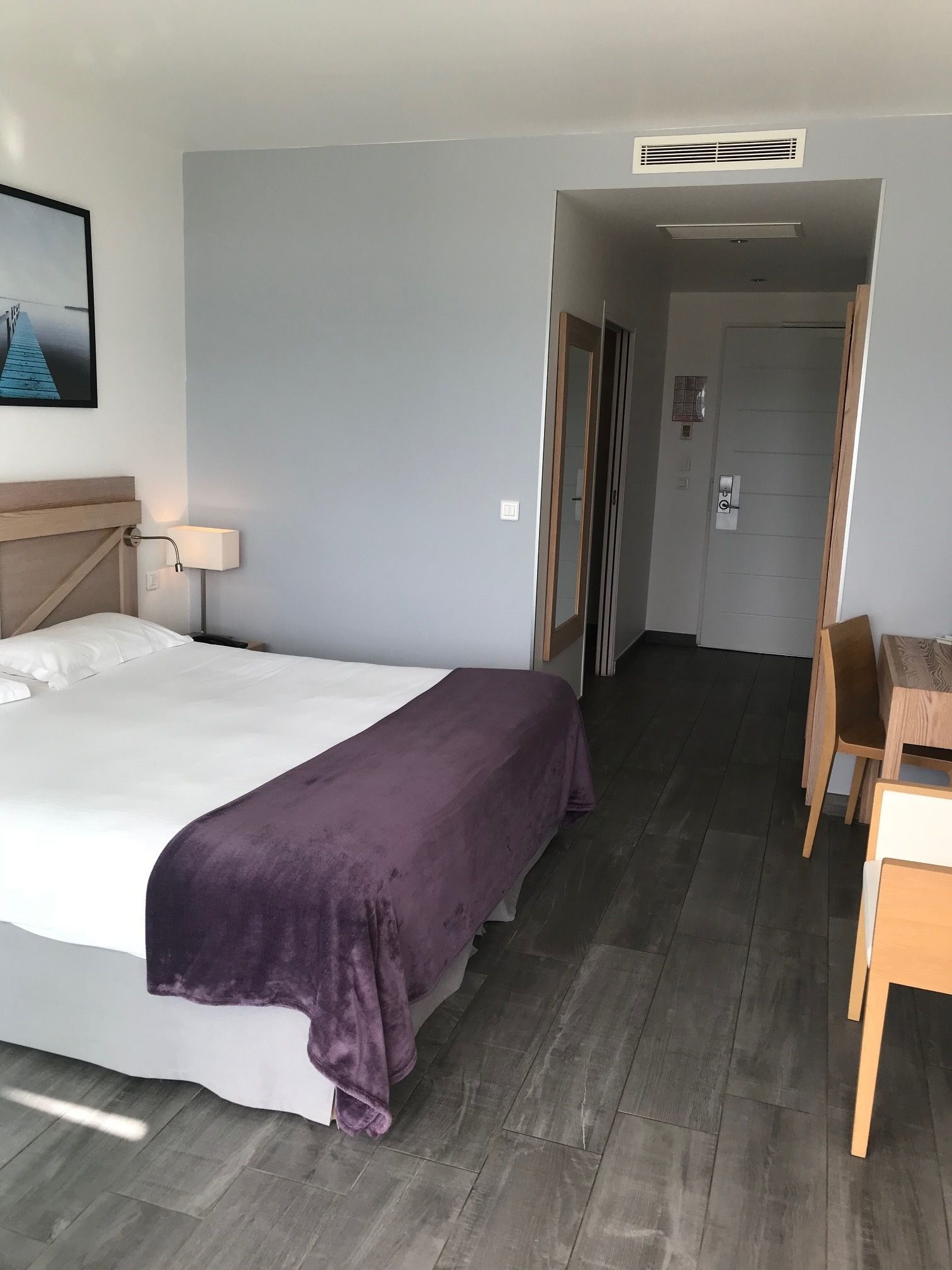 Une chambre d’hôtel avec un lit, un bureau et une chaise. Une porte donne accès à une autre pièce.