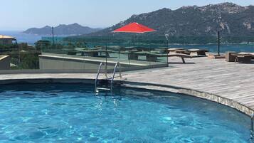 A swimming pool with a wooden deck, lounge chairs, and a red umbrella.