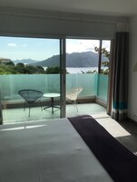 Balcón con vista a un cuerpo de agua y montañas, amueblado con dos sillas y una mesa.