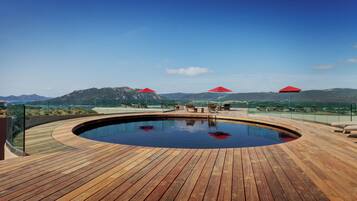 A wooden deck with a hot tub, red umbrellas, and a mountain view.
