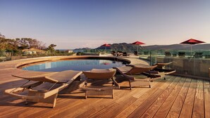 A poolside area with lounge chairs and red umbrellas, surrounded by glass railings and overlooking a mountainous landscape. - Hotel Carre Noir (Porto-Vecchio)