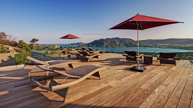 A wooden deck with lounge chairs and red umbrellas overlooking a scenic landscape. - Hotel Carre Noir (Porto-Vecchio)