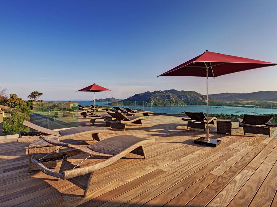 A wooden deck with lounge chairs and red umbrellas overlooking a scenic landscape.