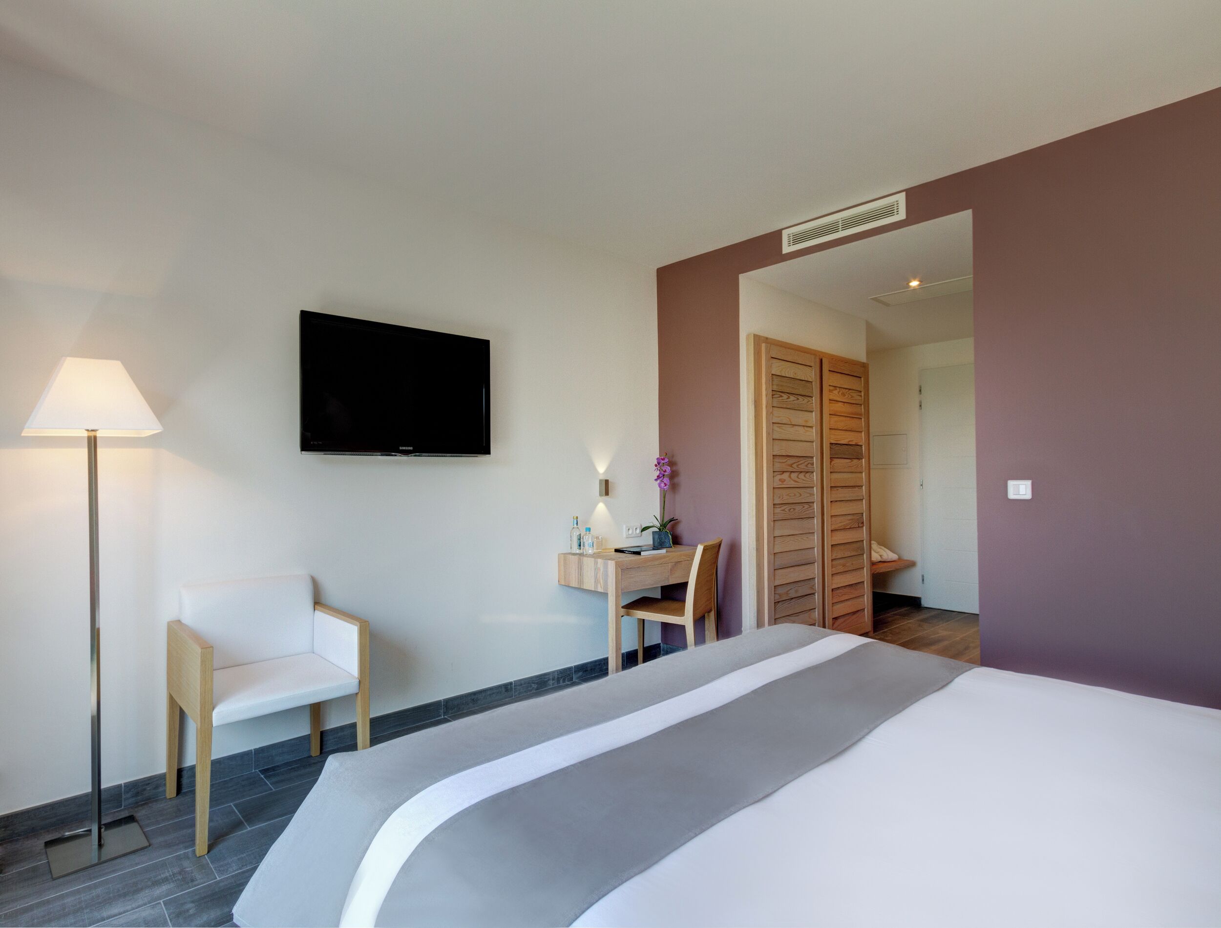 A hotel room with a bed, a desk, a chair, a TV, and a lamp.