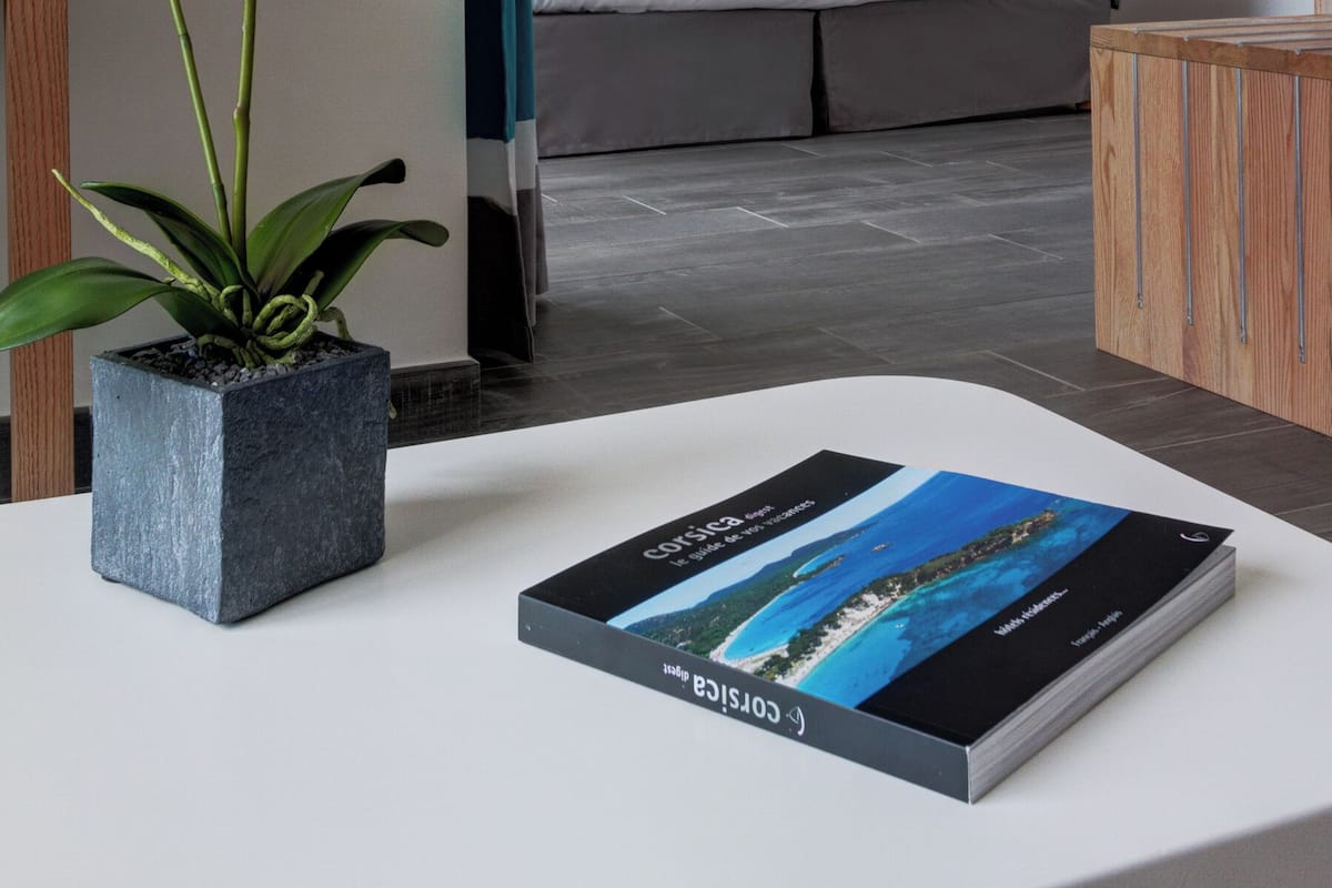 A hotel room with a bed, a nightstand, a potted orchid, and a book on the table.
