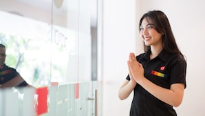 Une personne portant un t-shirt noir orné d’un logo, debout dans une pièce où se trouvent des casiers et une cloison en verre.