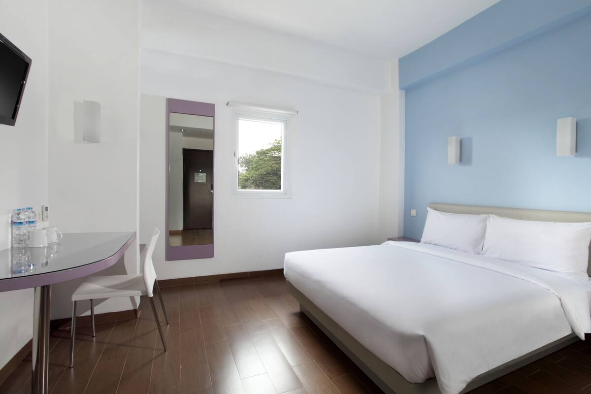 Ein Hotelzimmer mit einem Bett, einem Schreibtisch mit Stühlen, einem Fernseher und einem Fenster.