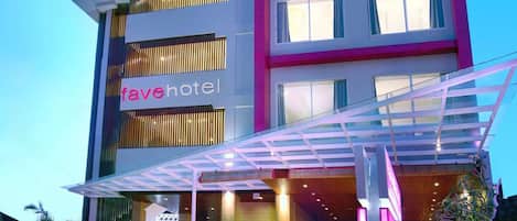 Un edificio de varios pisos con un letrero que dice 'fave hotel', con un diseño moderno, entrada de vidrio y palmeras frente a él.