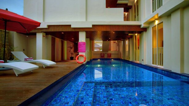 A swimming pool with lounge chairs and a red umbrella. - favehotel Kuta Square (Kuta)