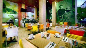 A modern restaurant with bright yellow and orange chairs, white tables, and a large mural on the wall. - favehotel Kuta Square (Kuta)