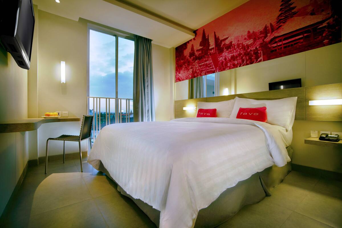 Une chambre d’hôtel avec un grand lit, un bureau avec une chaise, une télévision et un balcon avec vue.