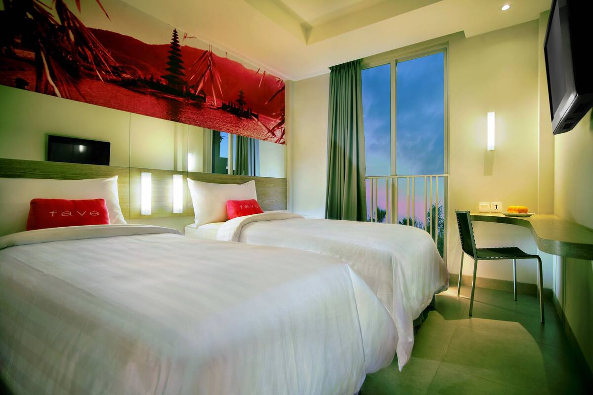 Une chambre d’hôtel avec deux lits, un bureau, une chaise, une télévision et une grande fenêtre.