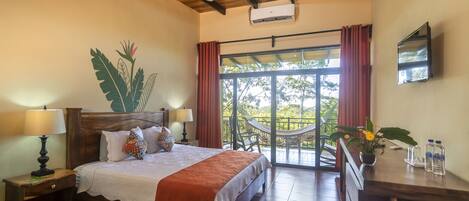 A bedroom with a bed, nightstands, a ceiling fan, a TV, a window with curtains, and a balcony with a chair.