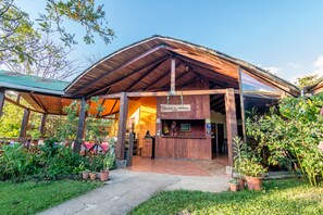 A wooden building with a covered entrance, potted plants, and a sign welcoming visitors.