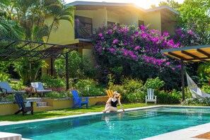 A pool area with a clear view of the pool, lounge chairs, and a building with a balcony.