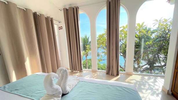 A hotel room with two beds, beige curtains, and a view of the ocean.