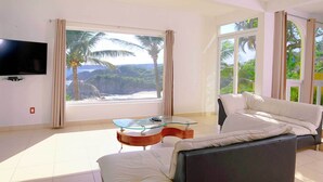 A modern living room with a large window, a glass coffee table, a sofa, and a TV mounted on the wall.