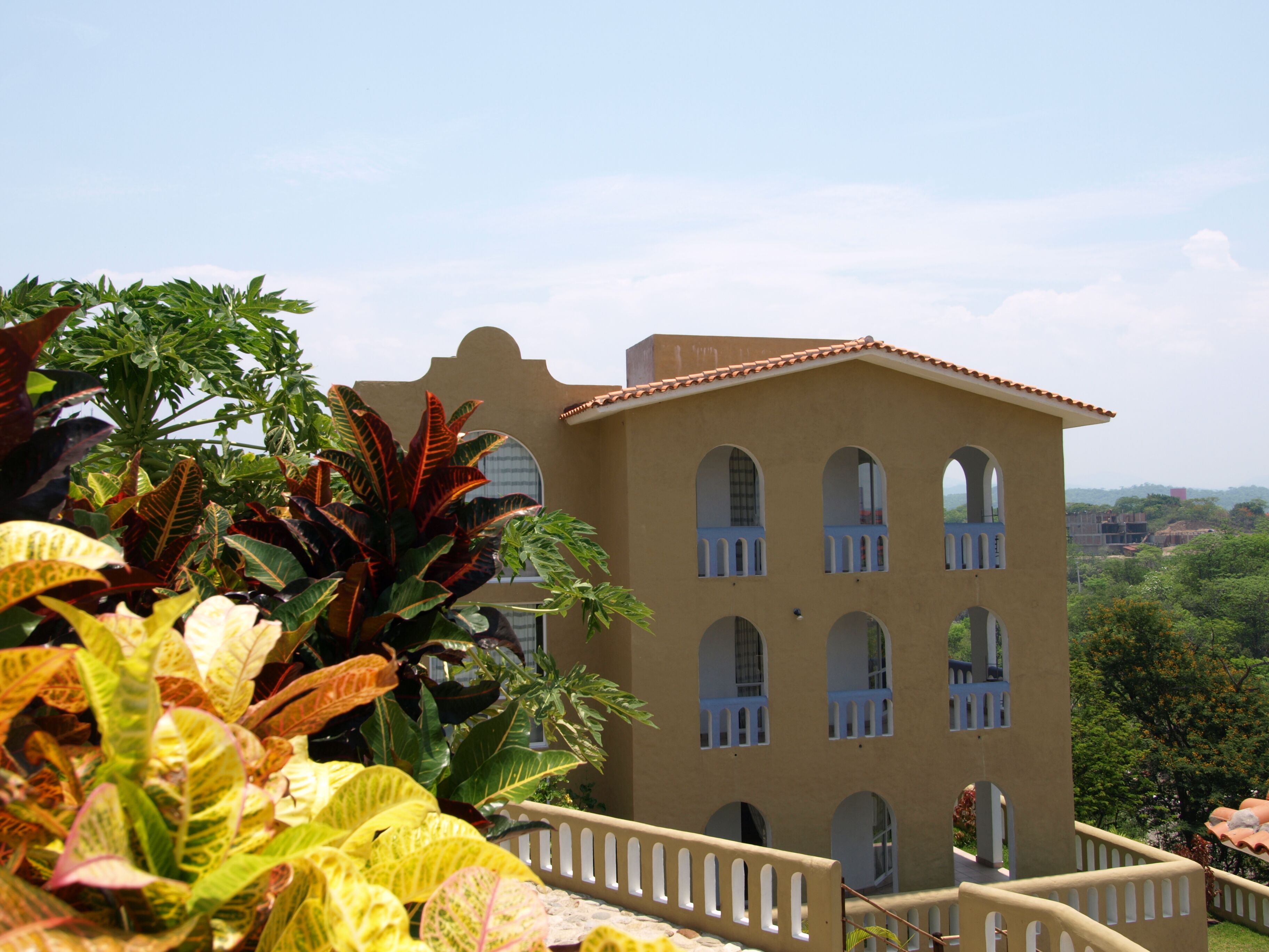A building with multiple arched windows and a balcony, surrounded by lush greenery.
