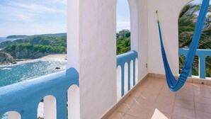 A balcony with a view of the ocean and cliffs, a blue hammock, and a white railing.
