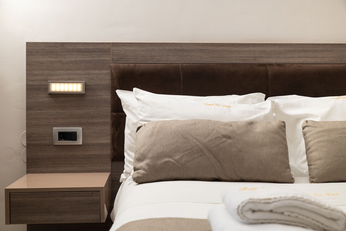 A neatly made bed with white and beige pillows, a wooden headboard, and a bedside table with a lamp.