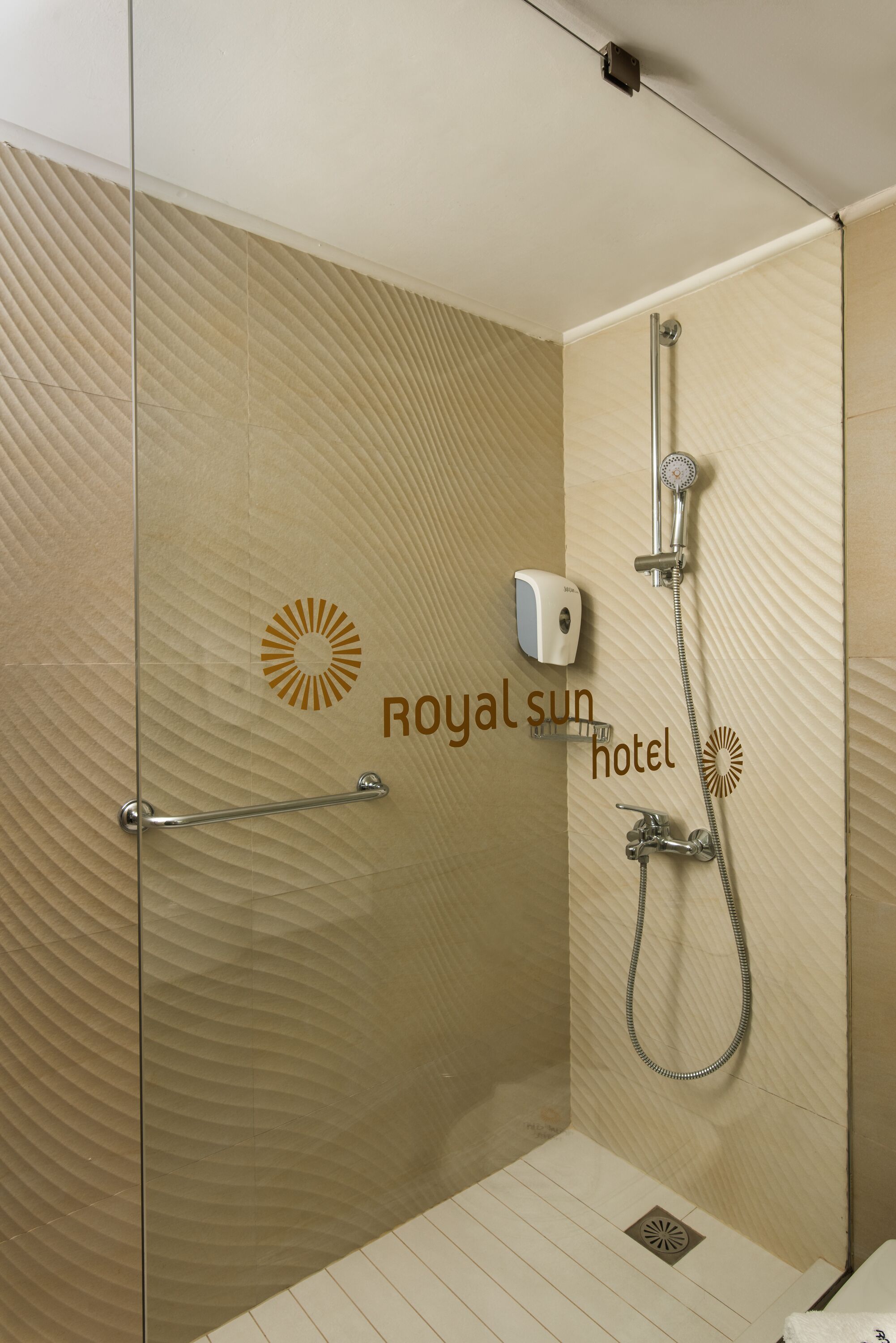 A shower area with a glass partition, a handheld showerhead, a handheld faucet, and a soap dispenser.