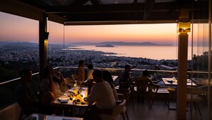 A restaurant with a view of a city and a body of water at sunset. - Royal Sun Hotel (Chania)