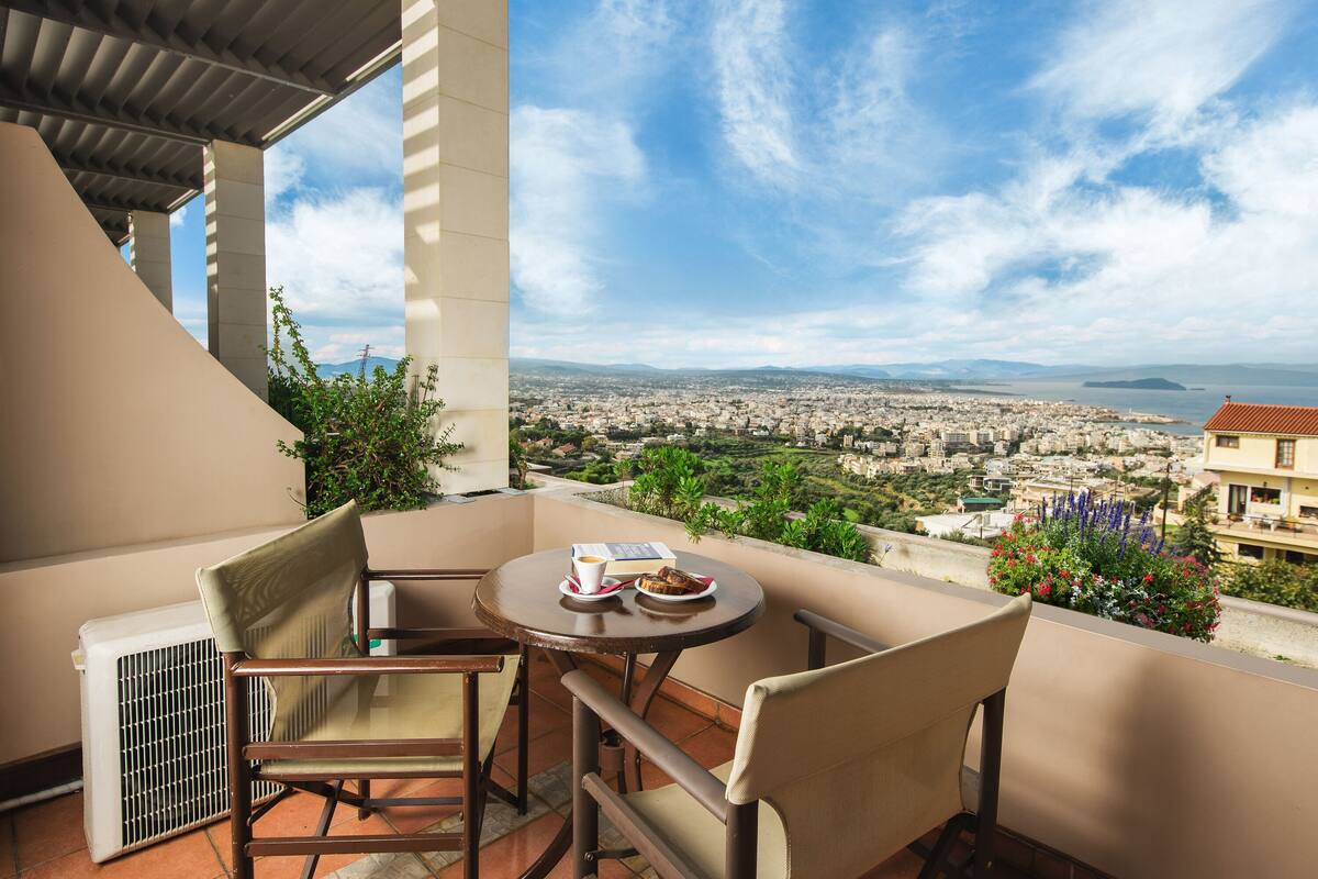 A balcony with a table, chairs, and a view of a cityscape and mountains.