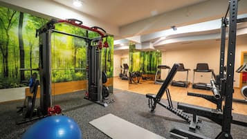 A gym with exercise equipment, a large exercise ball, and a wall mural of a forest.